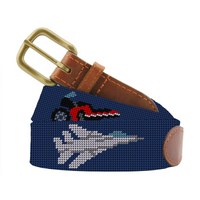 A navy blue hand-painted needlepoint canvas belt featuring a white fighter jet and a red and black motorcycle, with a brown leather strap and brass buckle.