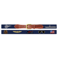 A navy blue embroidered belt with a brown leather strap and gold buckle, featuring embroidered military insignia, a fighter jet, an aircraft carrier, wings, a motorcycle, aviator sunglasses, and an American flag.